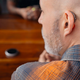 Looking at a man from the back with his head turned to the left and he's wearing a RIC hearing aid.