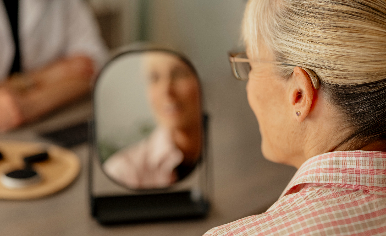 Woman looking in the mirror after being fit with hearing aids.