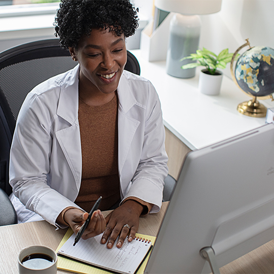 Professional looking at monitor and taking notes on notepad